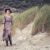 Blonde Frau steht am Strand mit einem modern Hippie Boho Look in Braun Weiß